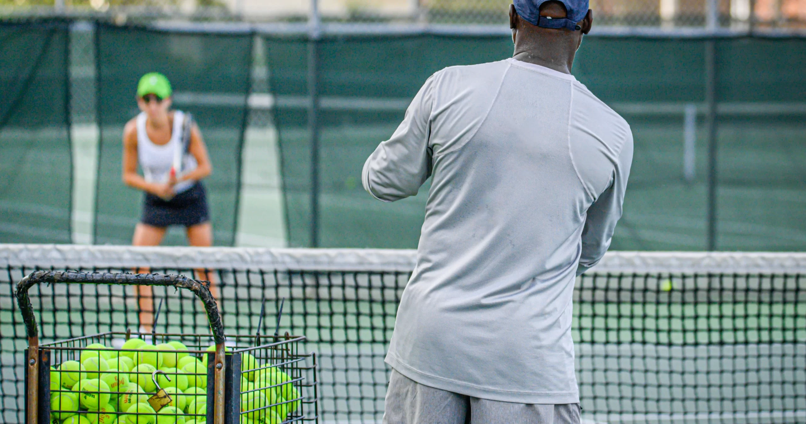 Tennis Coach with Blue Cap Feeding Balls to a Student